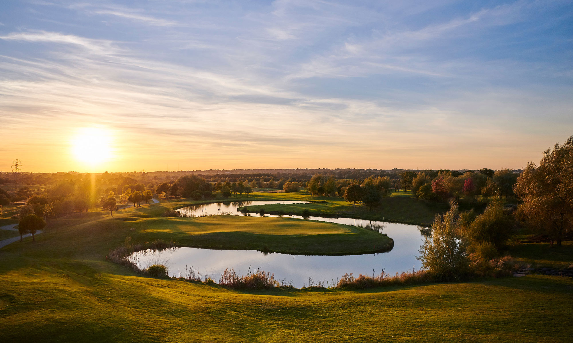 Aerial view of a golf course fairway winding around a pond at sunset